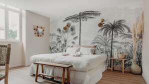 A bedroom with a bed, wooden bench, and a wall mural of palm trees. - Palmito (Biarritz)