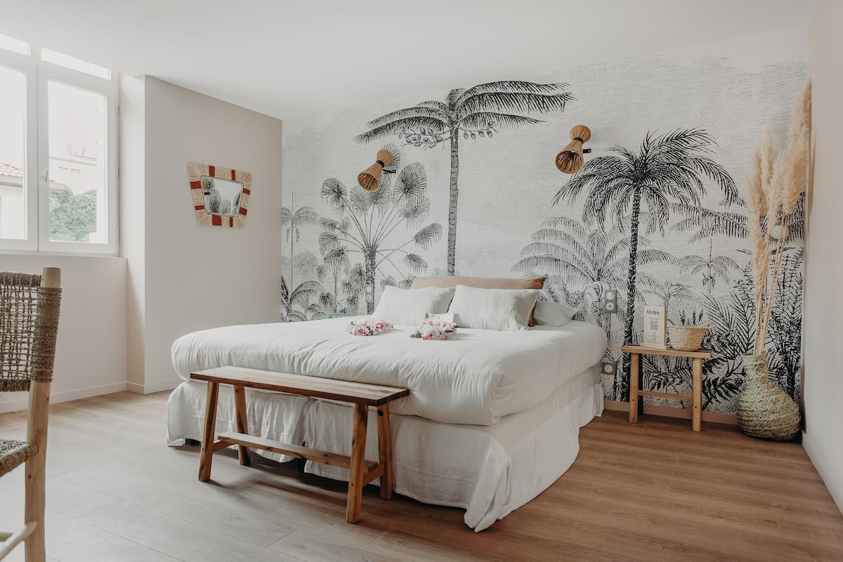 Un dormitorio con cama, banca de madera y un mural de palmeras.