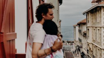 A narrow street with buildings on either side, a clear view of the sea, and a few pedestrians.
