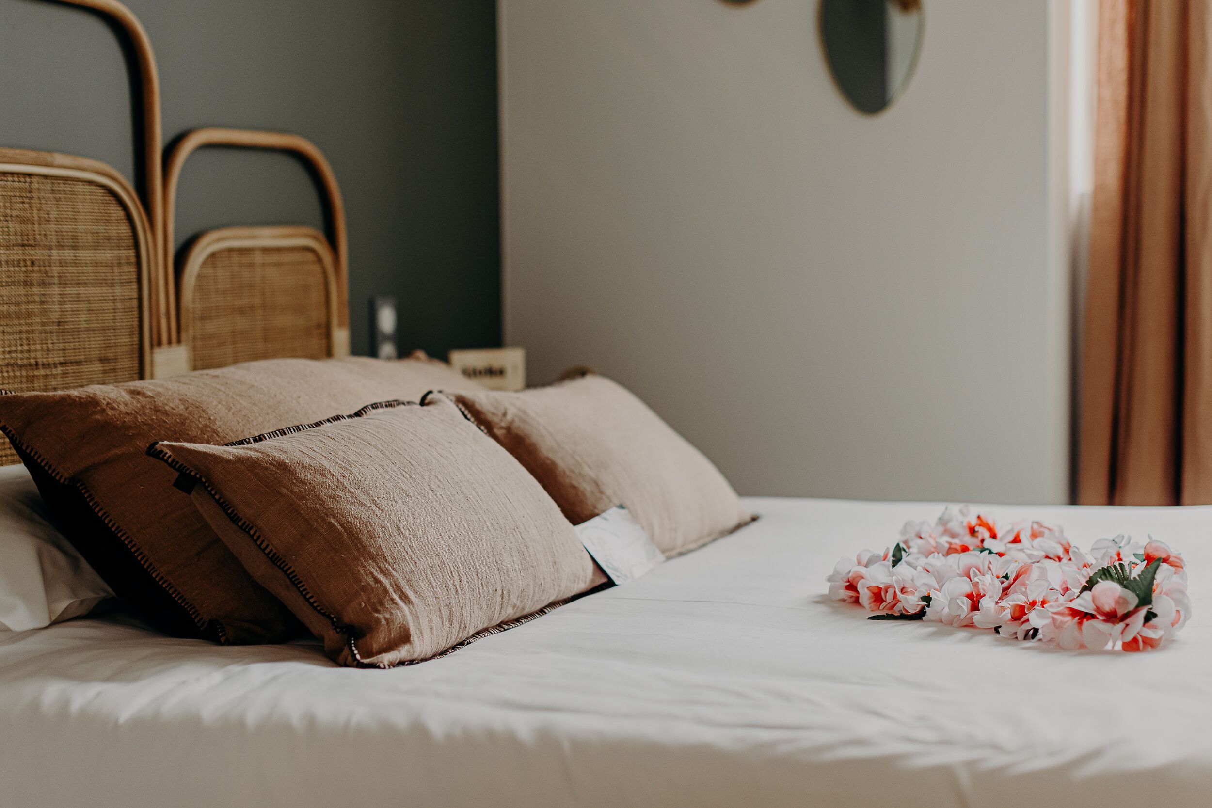 Een opgemaakt bed met twee kussens en een bloemstuk op een witte spreideken.