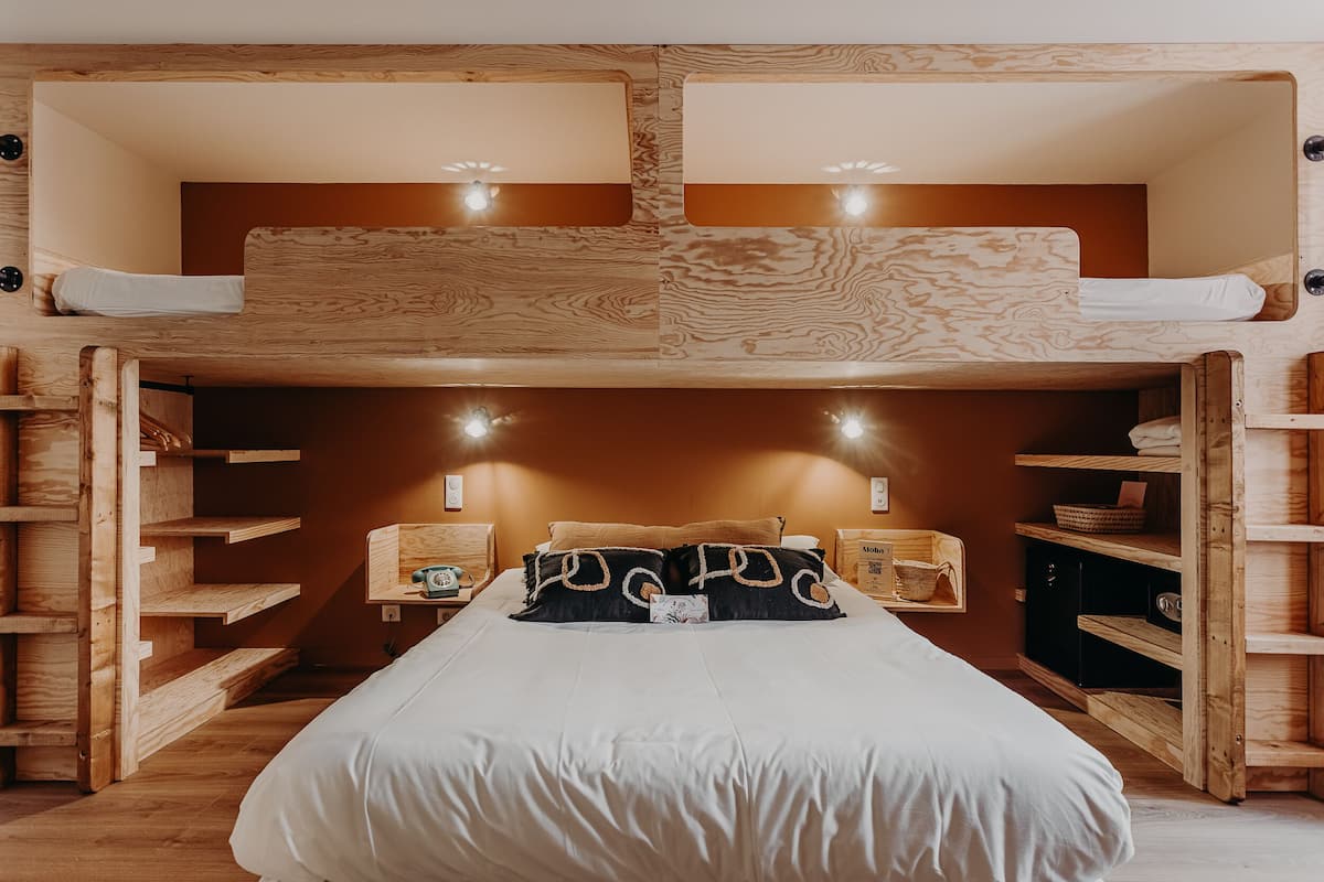 Una cama litera con cabecera de madera, mesitas de noche y estanterías empotradas.