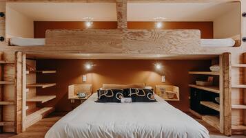 Una cama litera con cabecera de madera, mesitas de noche y estanterías empotradas.