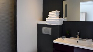 Une salle de bain moderne avec un mur foncé, un lavabo blanc et une pile de serviettes blanches posées sur une étagère.
