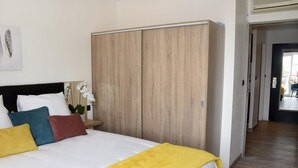 Une chambre d’hôtel avec un lit, une armoire en bois, une table de chevet avec une plante et une porte donnant sur une autre pièce.