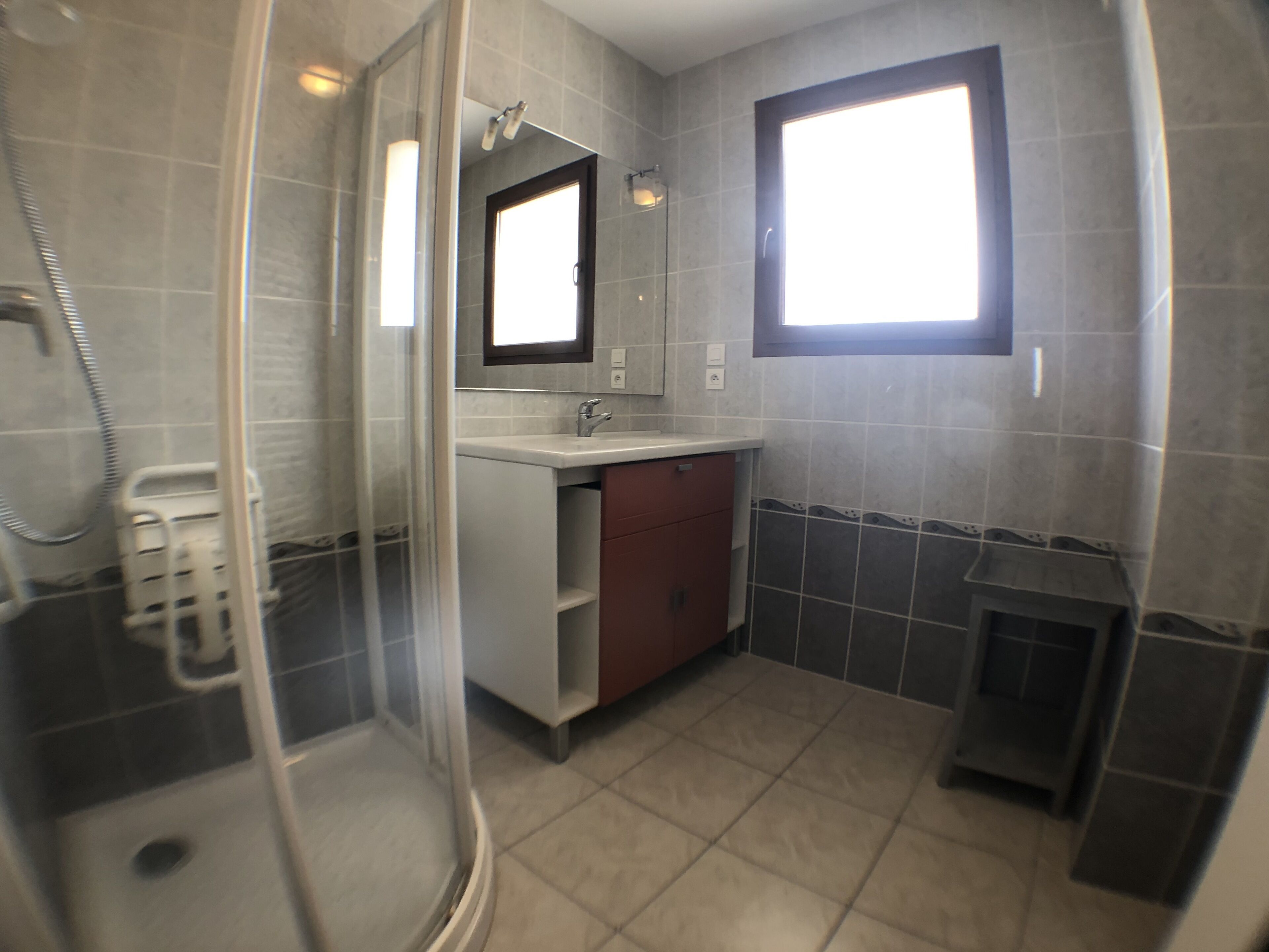Ein Badezimmer mit Duschkabine aus Glas, Waschbecken mit Spiegel und Fenster.