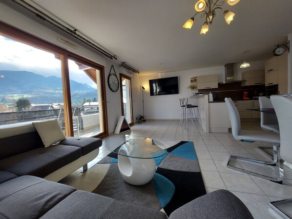 Uma sala de estar moderna com um sofá, uma mesa de centro de vidro e vista para montanhas através de grandes janelas.