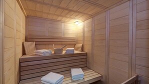 Una sauna con bancos y escalones de madera, toallas y una lámpara.