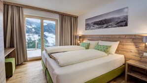 Una cama doble con cabecera tapizada de verde, una mesita de noche de madera, una lámpara de pared y una ventana con cortinas.