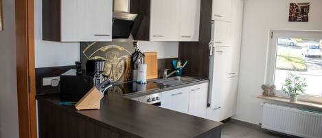 A modern kitchen with a central island, stainless steel appliances, and a window with a view of the street.