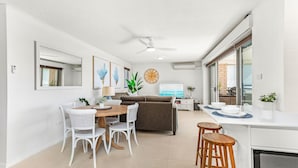 A modern kitchen with a dining area, white walls, and a large window. - Waves on North - El Sandi 4 (Forster)