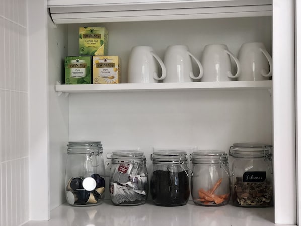 A kitchen shelf with tea boxes, white mugs, and jars of tea bags and spices. - Waves on North - El Sandi 4 (Forster)