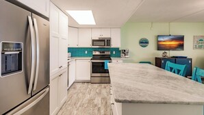 Una cocina moderna con armarios blancos, un refrigerador de acero inoxidable, un microondas y una isla grande con sillas azules.