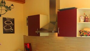 Una cucina compatta con mobili rossi, un lavandino in acciaio inossidabile e una macchina da caffè sul piano di lavoro.