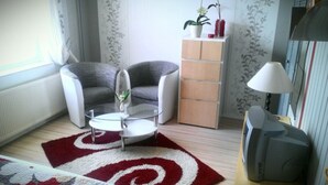 Un soggiorno moderno con una poltrona grigia, un tavolino bianco e un tappeto rosso e bianco. Si nota un mobile in legno e una lampada su un tavolo.