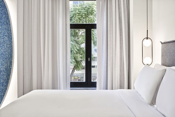 Habitación de hotel con cama, vista a través de un ventanal y una lámpara colgante.
