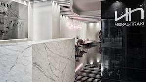 Un hall d’hôtel moderne avec un comptoir d’accueil en marbre, un mur noir orné du nom de l’hôtel et un escalier doté d’un revêtement de sol réfléchissant.