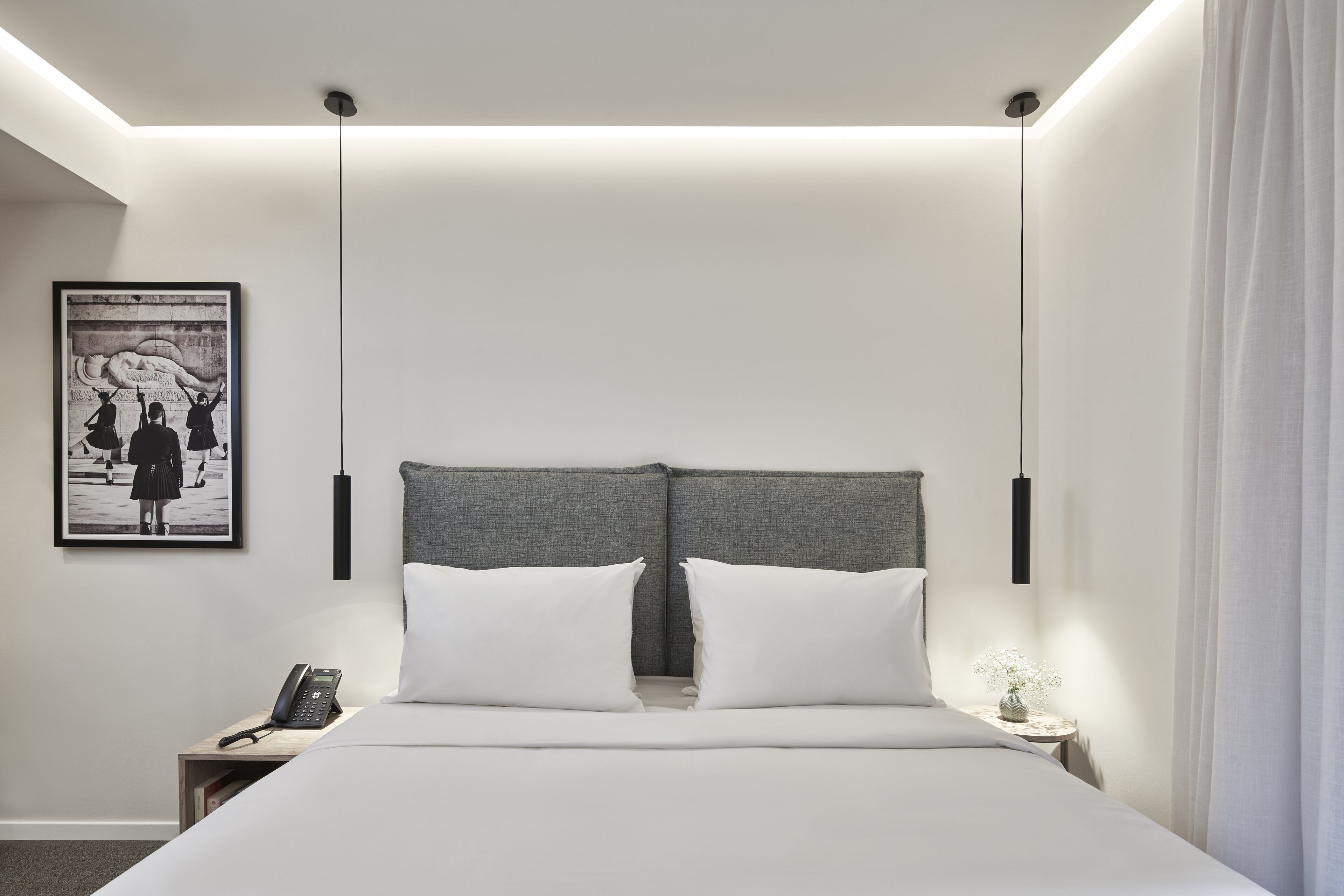 A modern hotel room with a large bed, a bedside table with a phone, and a framed artwork on the wall.