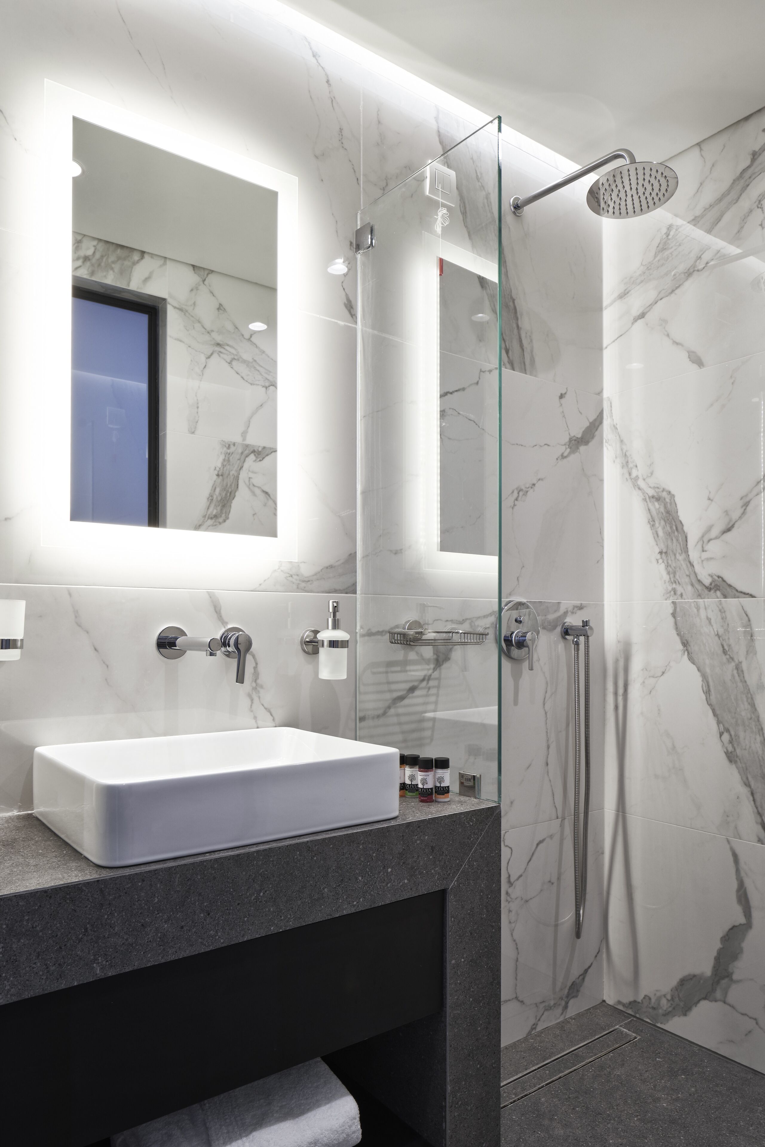 A modern bathroom with a marble sink, a glass-enclosed shower, and a large mirror.