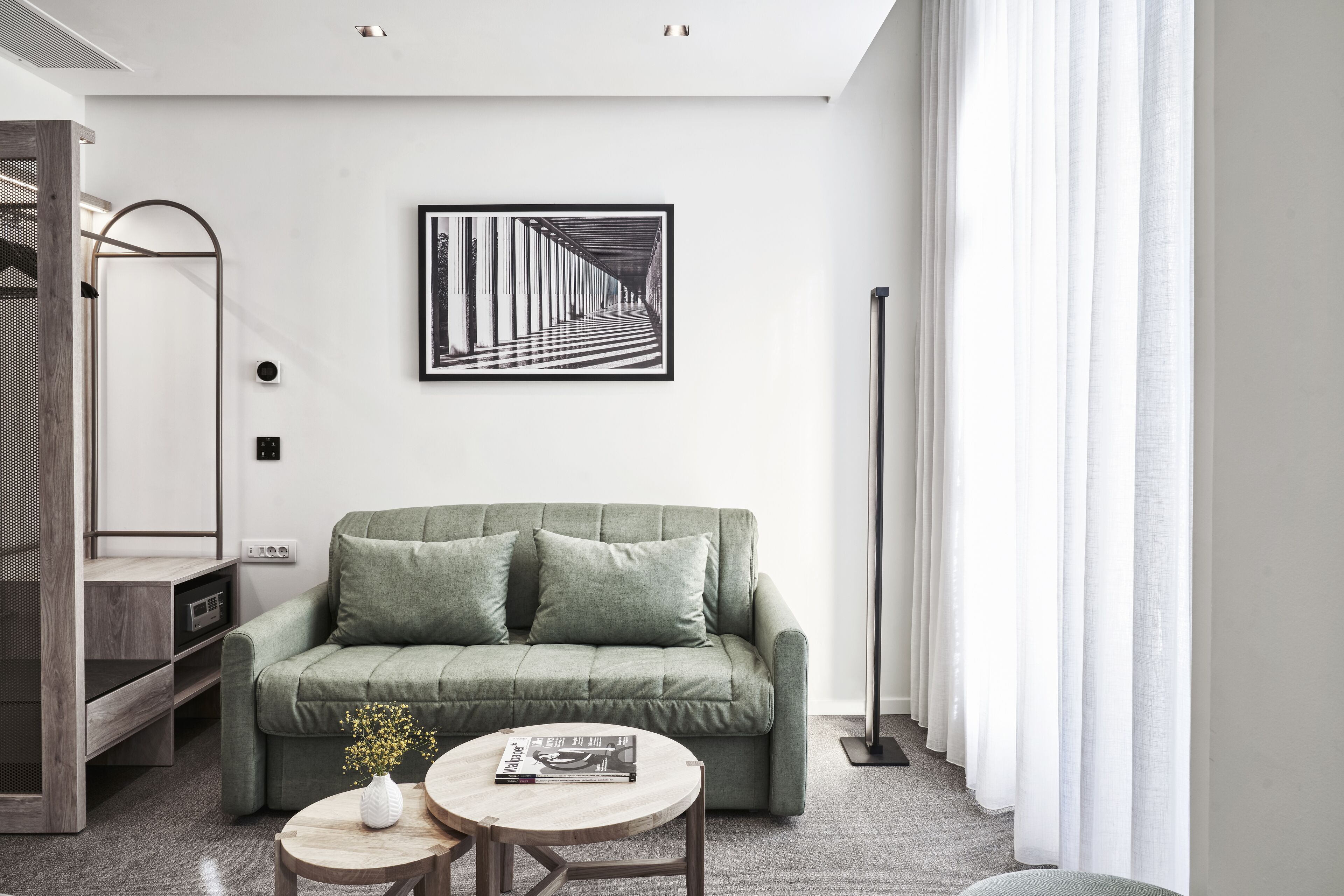 A modern living room with a green sofa, a round wooden coffee table, and a framed black and white artwork on the wall.