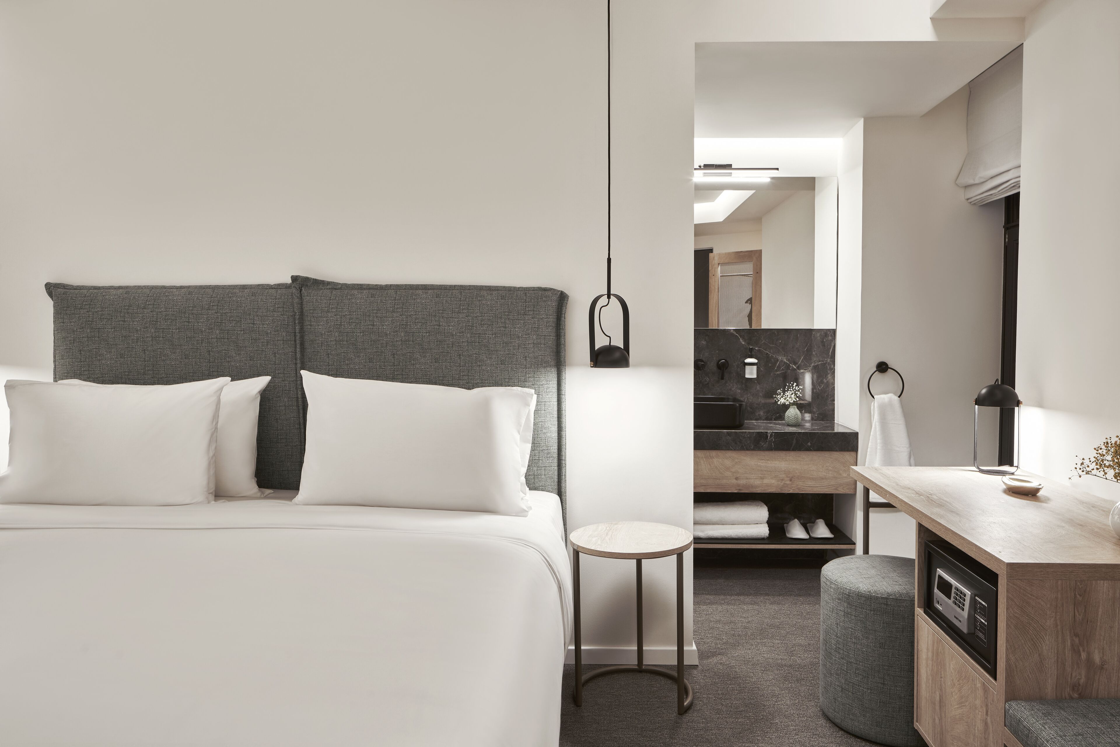 A modern hotel room with a large bed, a small round table, a built-in microwave, and a vanity with a mirror.