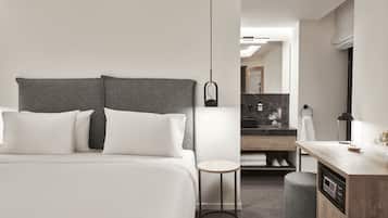 A modern hotel room with a large bed, a small round table, a built-in microwave, and a vanity with a mirror.