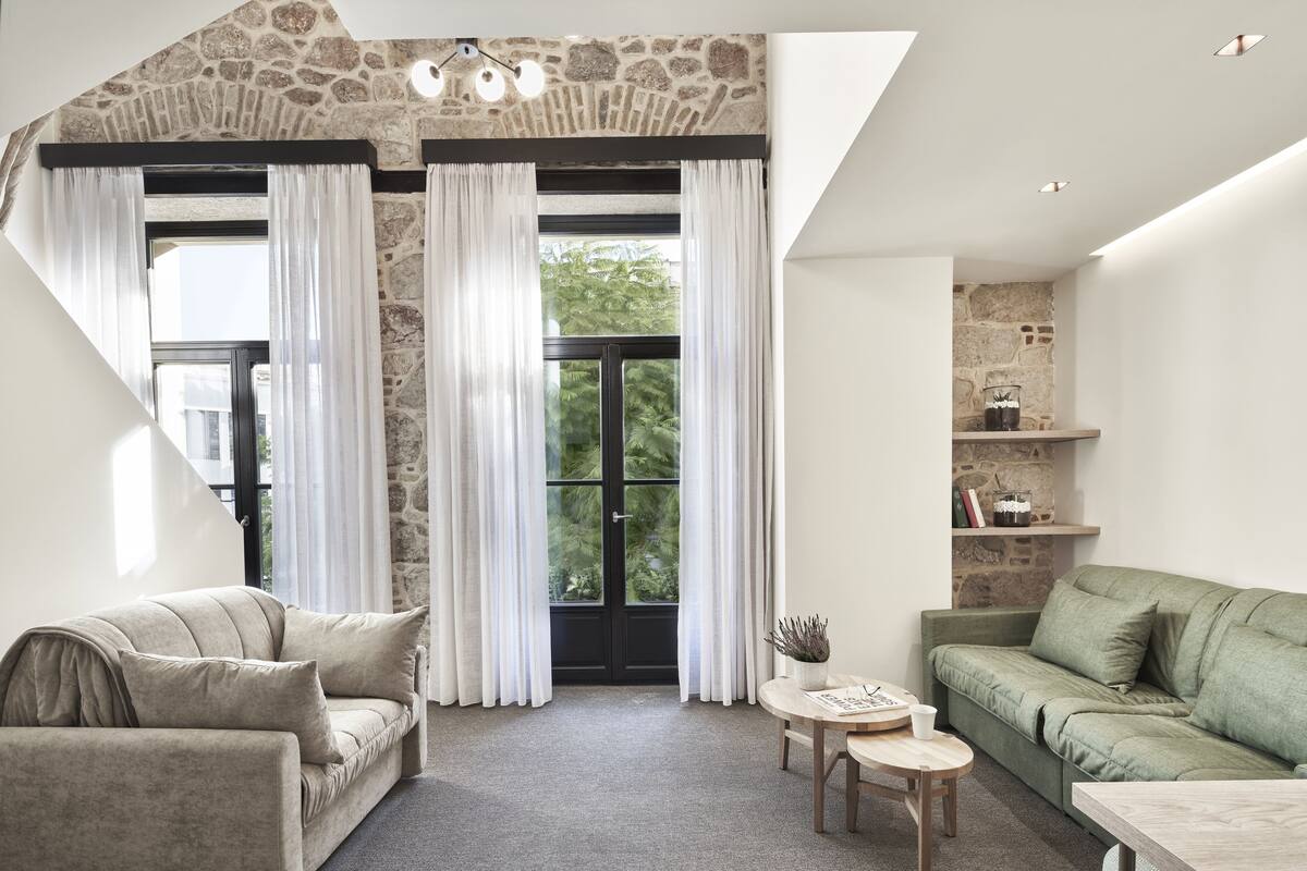 Una sala de estar moderna con una pared de acento de piedra, un sofá verde, un sofá beige y una pequeña mesa de madera.
