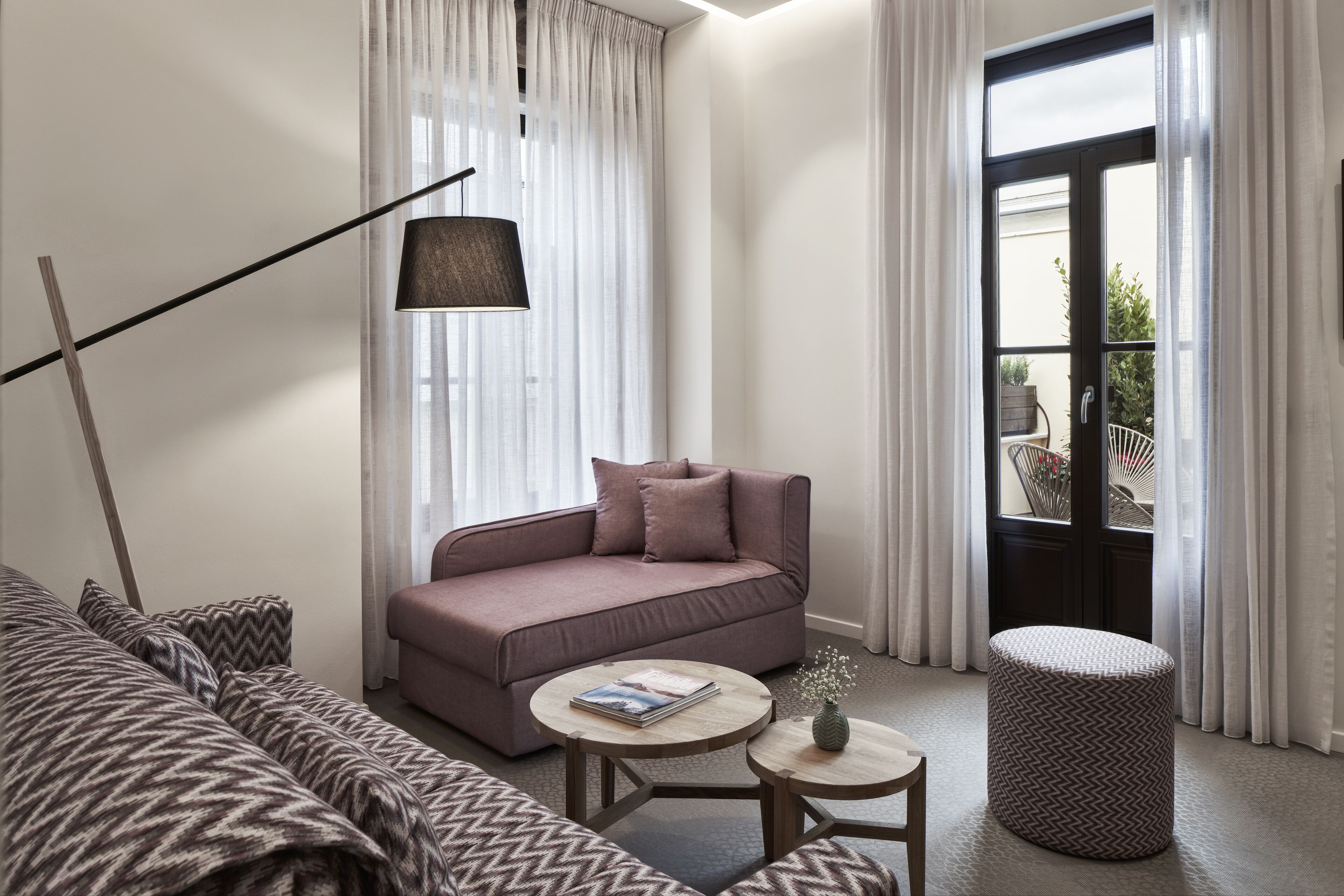A modern living room with a sofa, a round coffee table, a lamp, and a view of the outdoors through a door.
