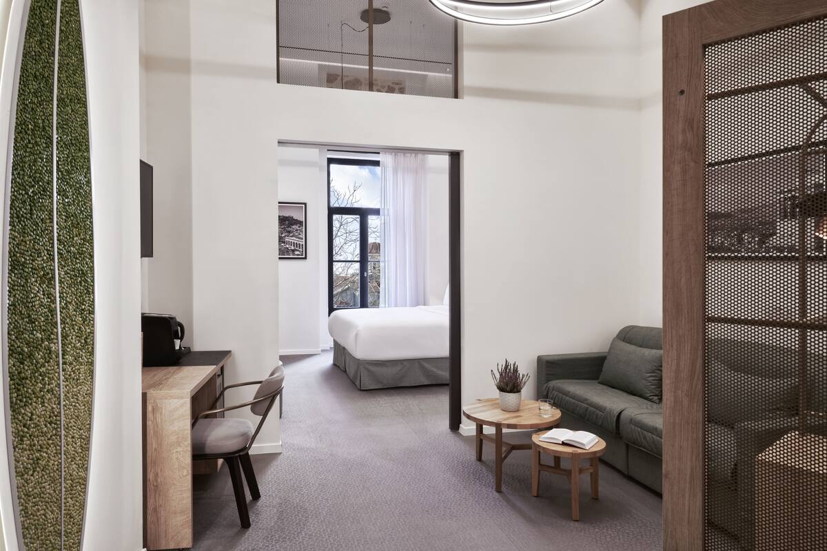 Una habitación de hotel moderna con una cama, un escritorio, una silla, un sofá y una pequeña mesa con una planta.