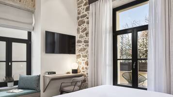 A bedroom with a stone accent wall, a large window with curtains, a bedside table with a lamp, a chair, and a TV mounted on the wall.
