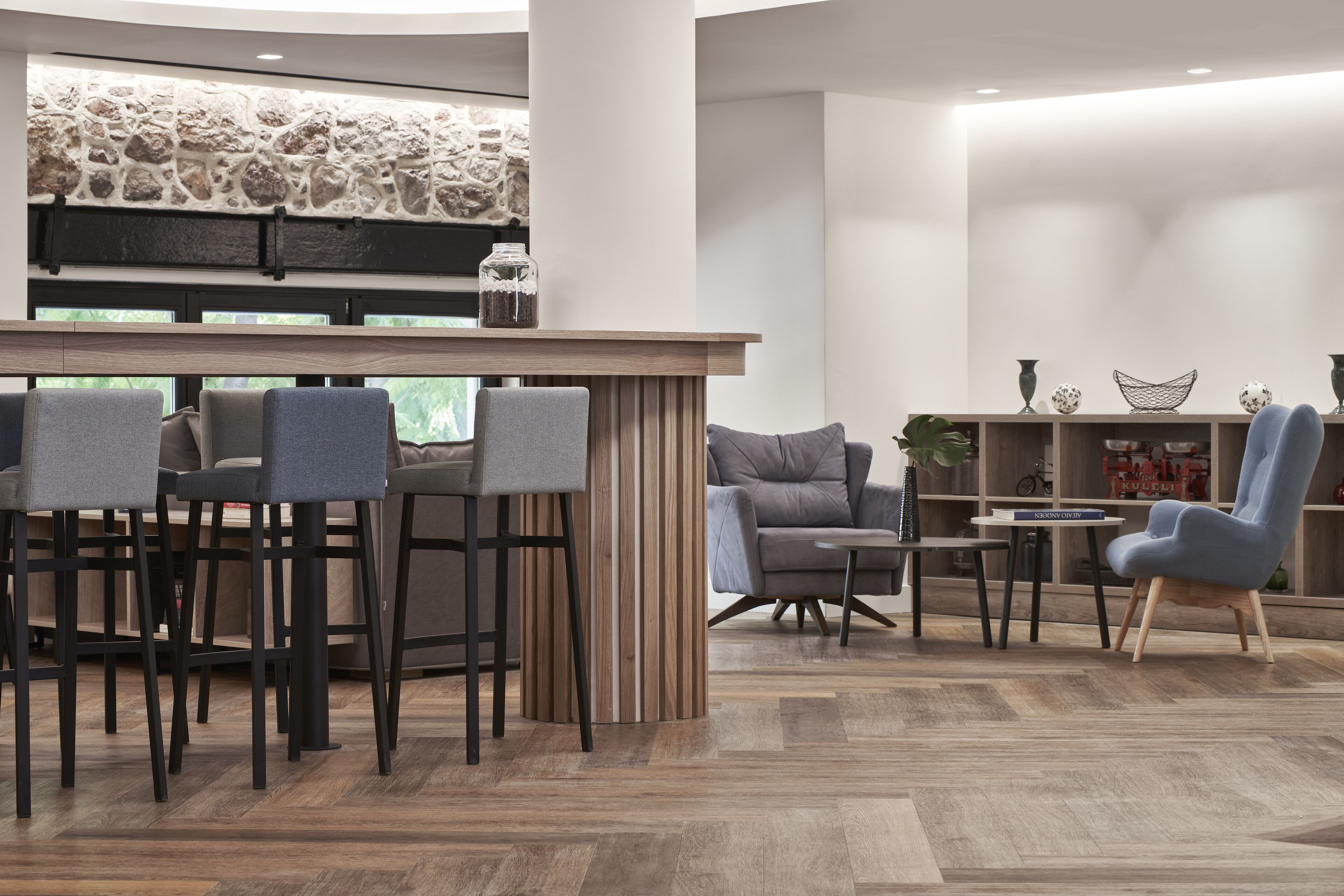 A modern bar area with a stone wall, bar stools, and a seating area with a sofa and armchairs.