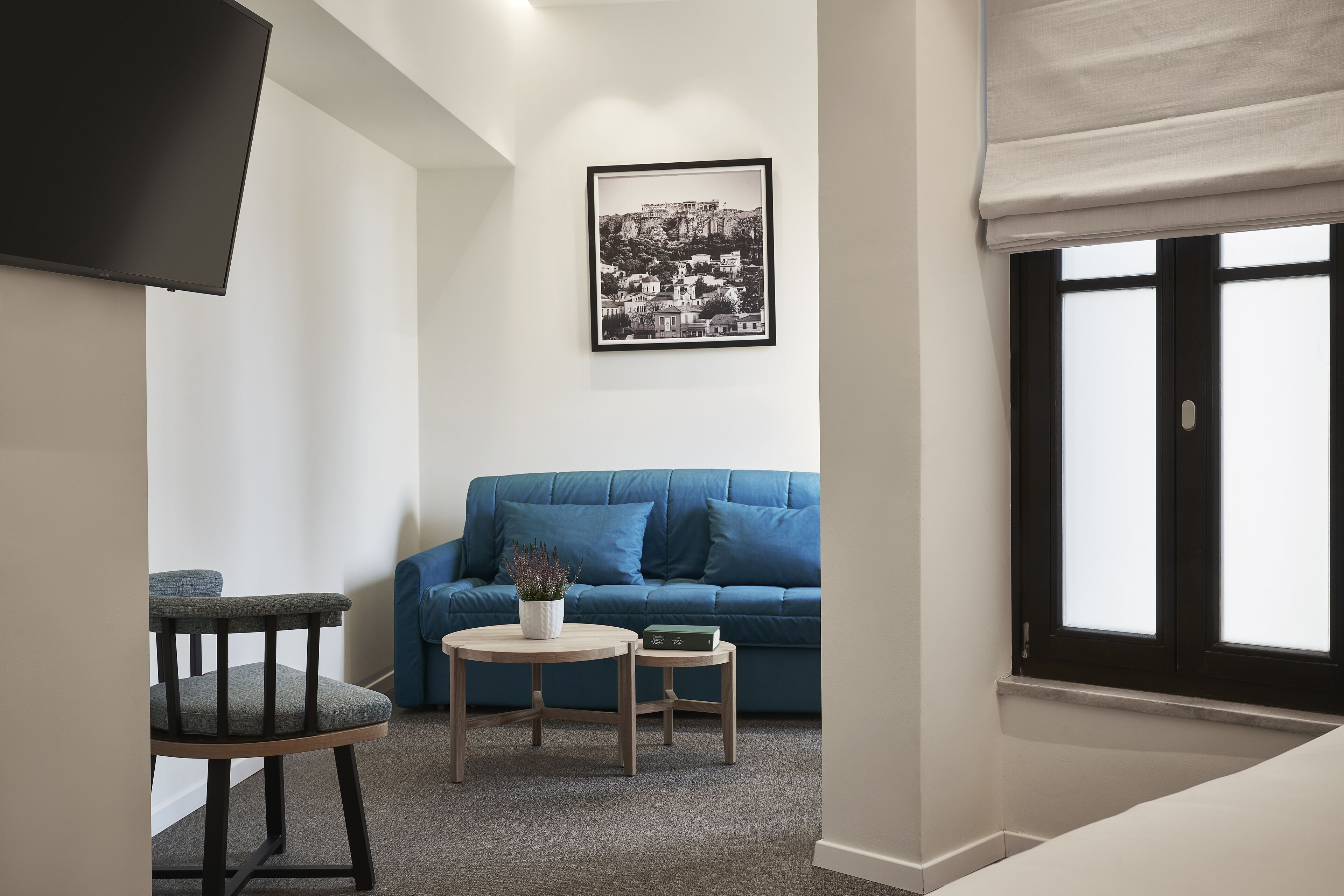 Un salón con un sofá azul, una pequeña mesa redonda con una planta y un cuadro en la pared.