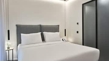Una habitación de hotel moderna con una cama grande, una mesita de noche y un pequeño jarrón con flores.