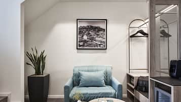 A modern room with a large potted plant, a blue armchair, a coffee table with a magazine, a framed cityscape photo, and a wardrobe with a hanging rack.