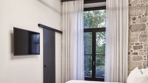 Une chambre moderne avec un mur d’accent en pierre, un grand lit, un téléviseur à écran plat et un luminaire circulaire au plafond.