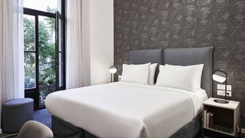 A hotel room with a large bed, two bedside lamps, a nightstand, and a view of greenery through a window.