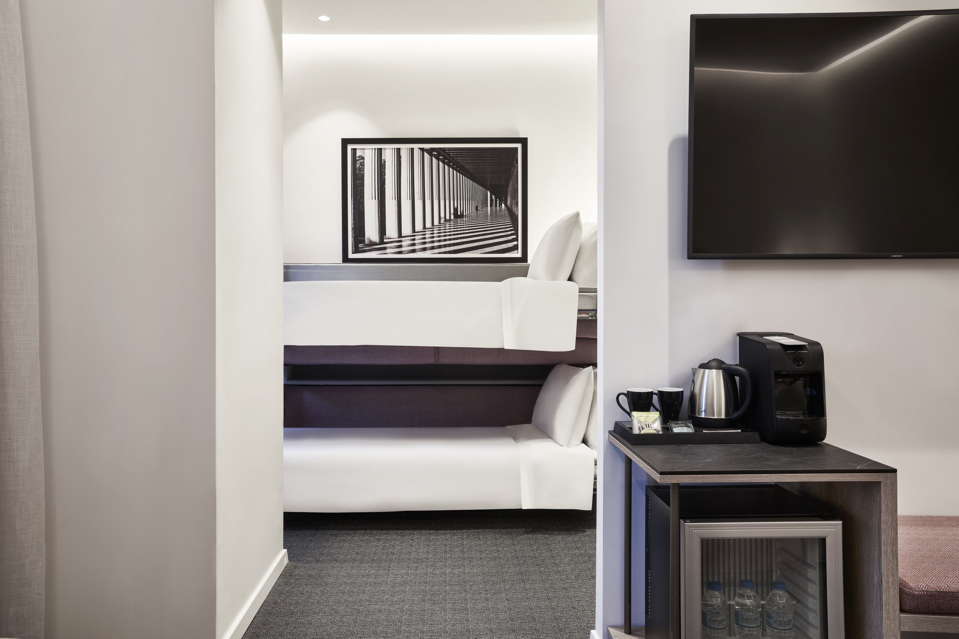 Ein modernes Hotelzimmer mit Etagenbett, Flachbildfernseher, Kaffeemaschine und einem kleinen Kühlschrank.