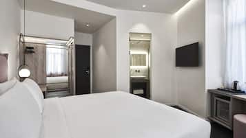 A modern hotel room with a large bed, a desk with a flat-screen TV, a bathroom with a mirror and sink, and a walk-in closet.