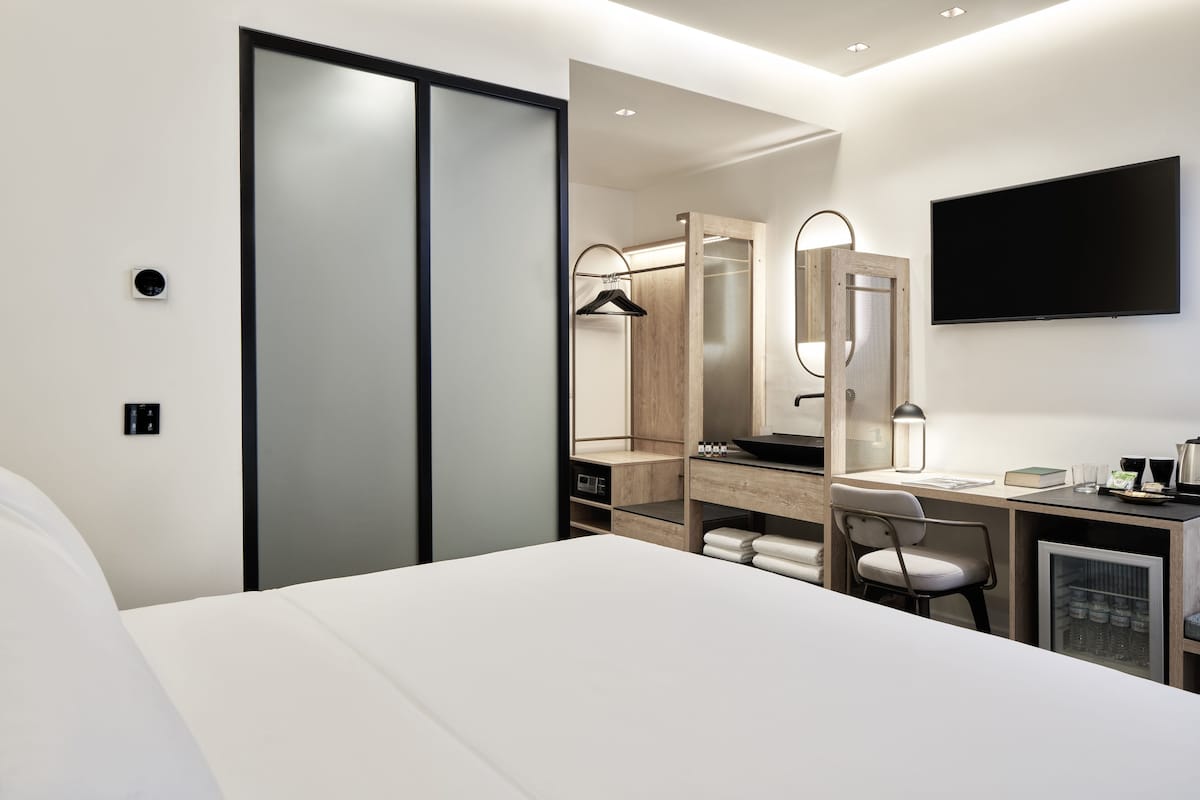 Habitación de hotel moderna con una cama grande, un escritorio con silla, armario, espejo y televisor en la pared.