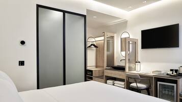 Habitación de hotel moderna con una cama grande, un escritorio con silla, armario, espejo y televisor en la pared.