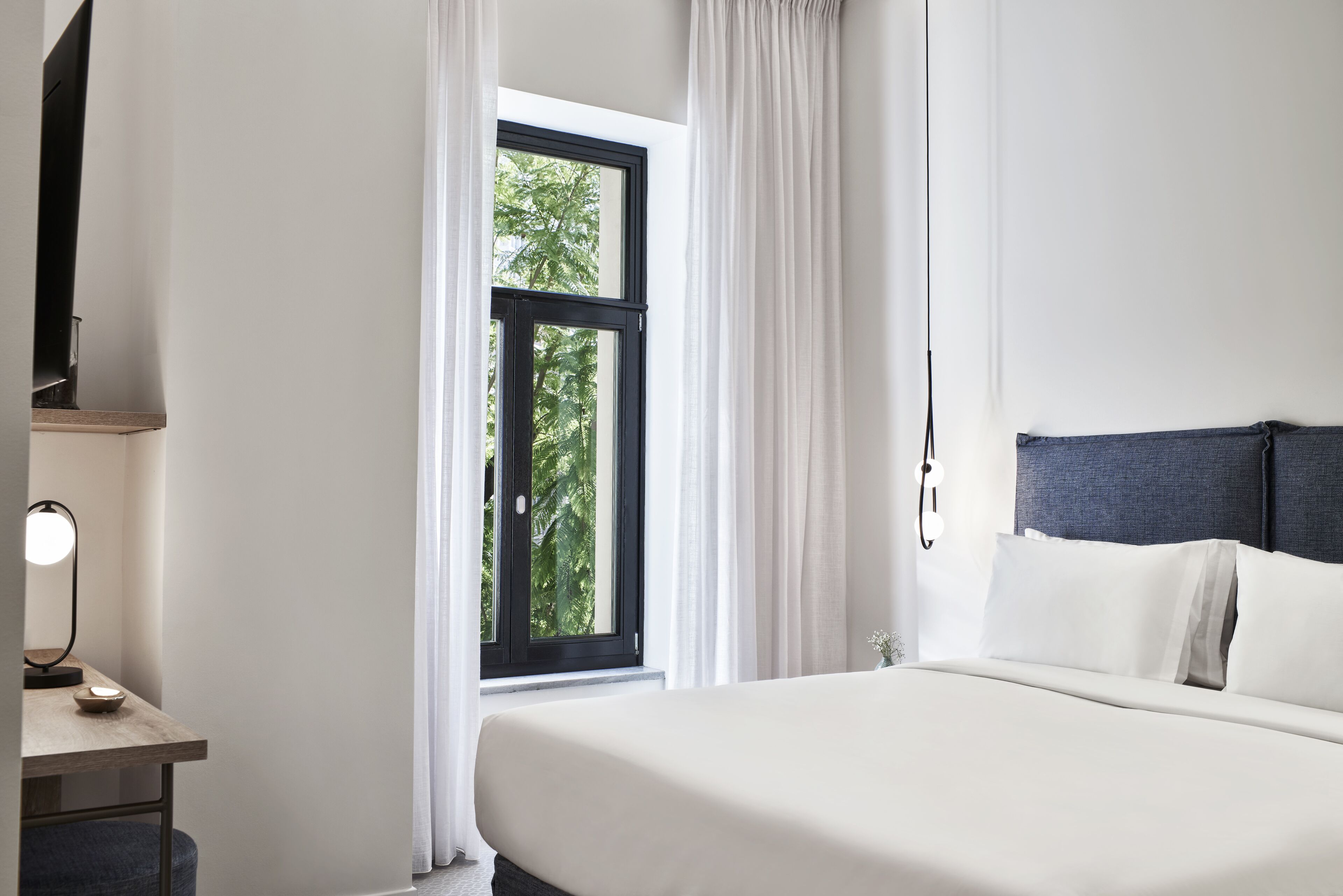 A bedroom with a bed, a desk with a lamp, and a window with curtains.