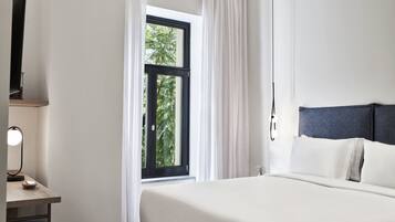A bedroom with a bed, a desk with a lamp, and a window with curtains.