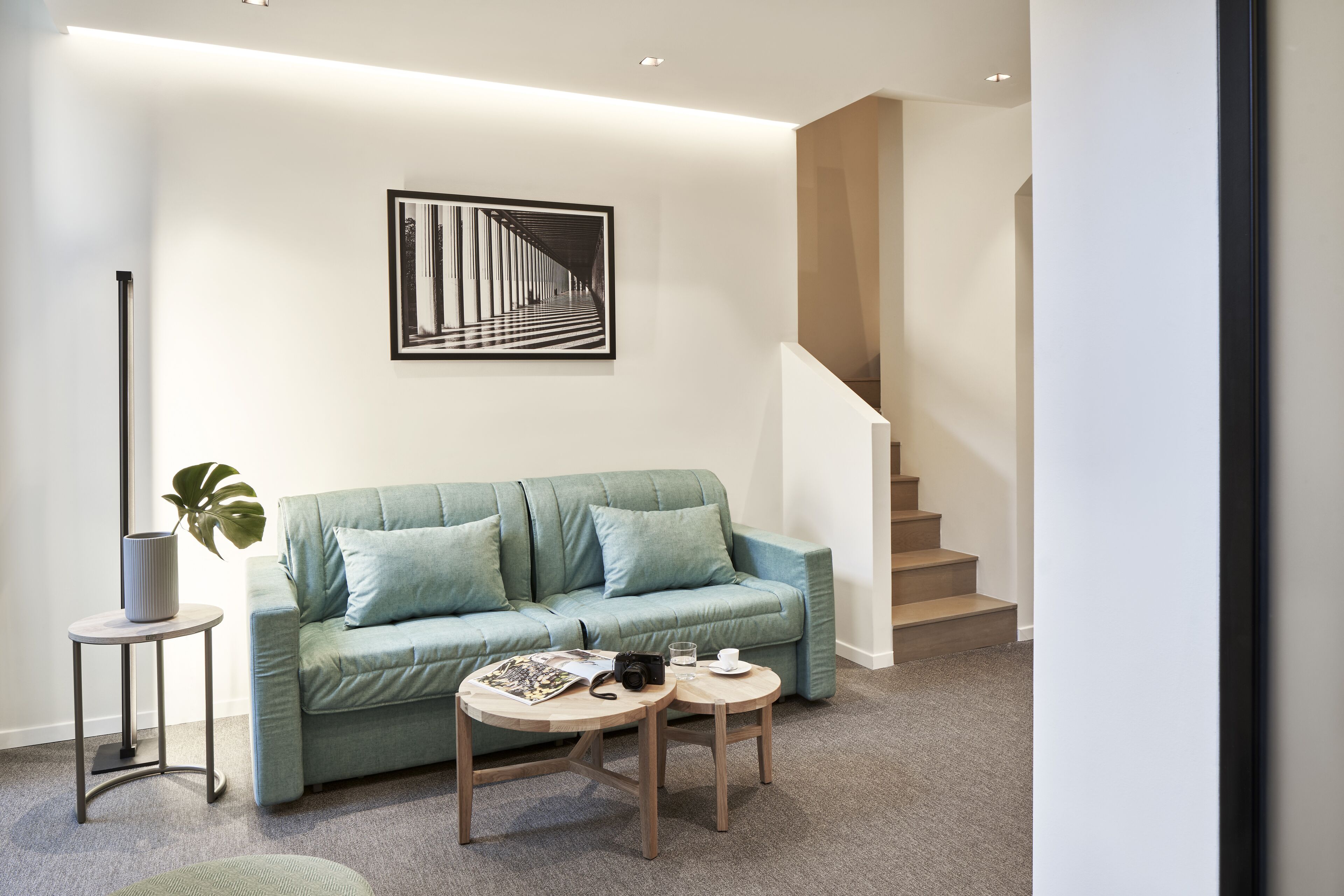 A modern living room with a teal sofa, a coffee table, and a framed artwork on the wall.
