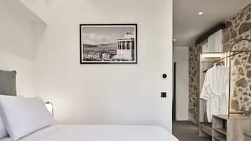 A bedroom with a bed, a framed picture of a historical building, a closet with a robe, and a stone wall.