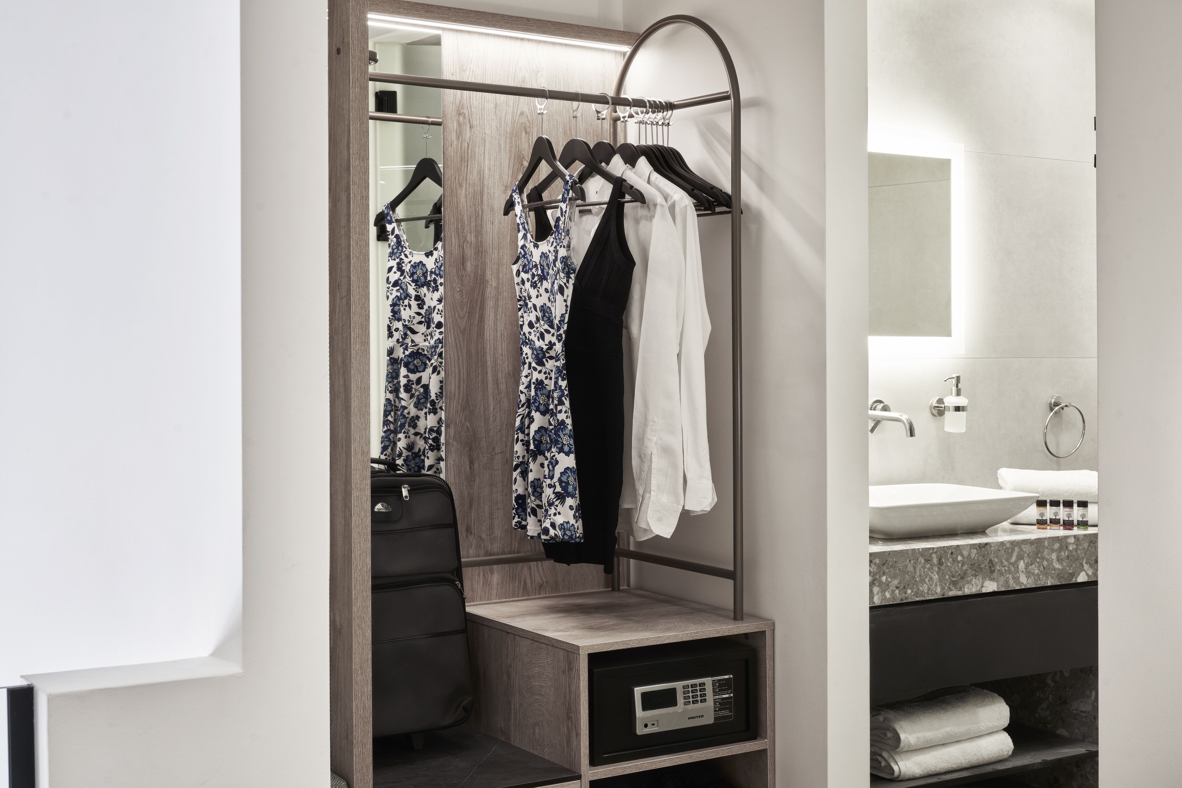 Ein modernes Badezimmer mit einem Holzbadezimmerschrank, einem Spiegel, einem Waschbecken und einem Wäscheständer mit Kleidung.