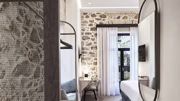 A modern hotel room with a stone accent wall, a desk with a chair, a bed, and a large mirror.