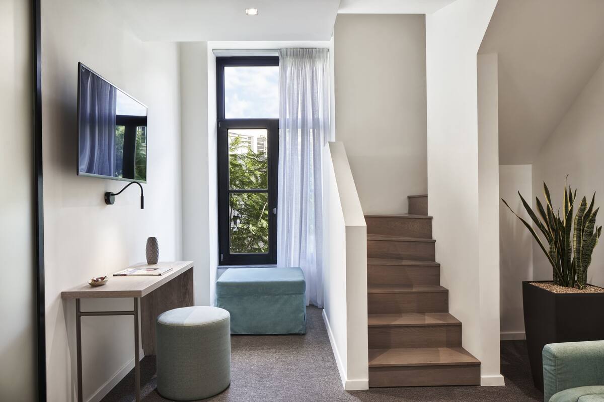 Un interior moderno con una escalera, un televisor de pantalla plana montado en la pared, un escritorio con un florero y una planta en maceta.