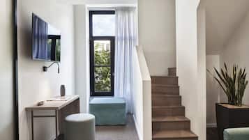 Un interior moderno con una escalera, un televisor de pantalla plana montado en la pared, un escritorio con un florero y una planta en maceta.