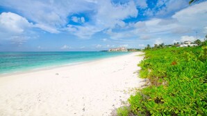 Una spiaggia con sabbia bianca, acqua cristallina turchese e alcuni edifici in lontananza.