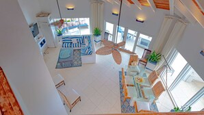 Un'ampia zona giorno con soffitto alto, grandi finestre e ventilatore a soffitto.