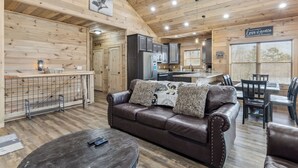 Interior acogedor de una cabaña con techo de madera, un sofá de cuero, un comedor y una cocina.